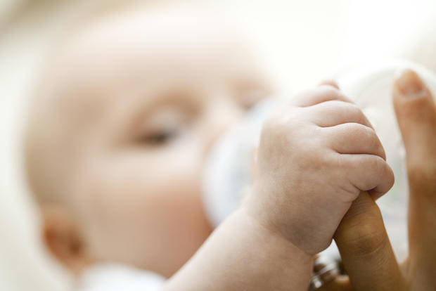 Baby drinking from bottle and holding mother's finger, close-up 