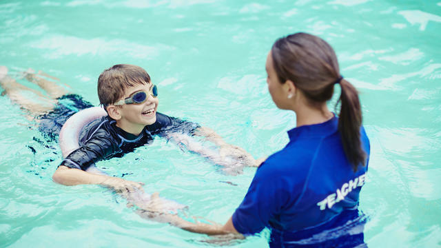 Young boy learning to swim in pool with teacher 