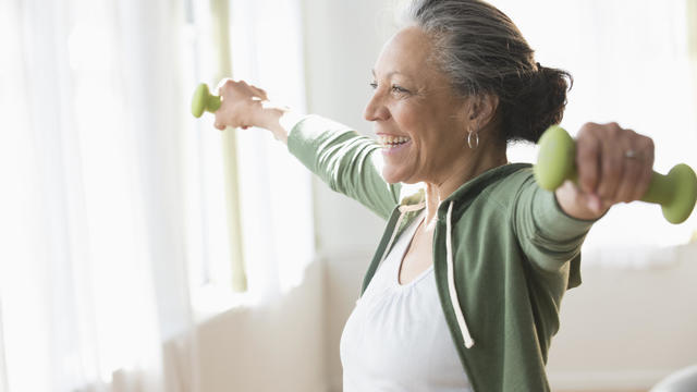 Older Hispanic woman lifting weights in living room 