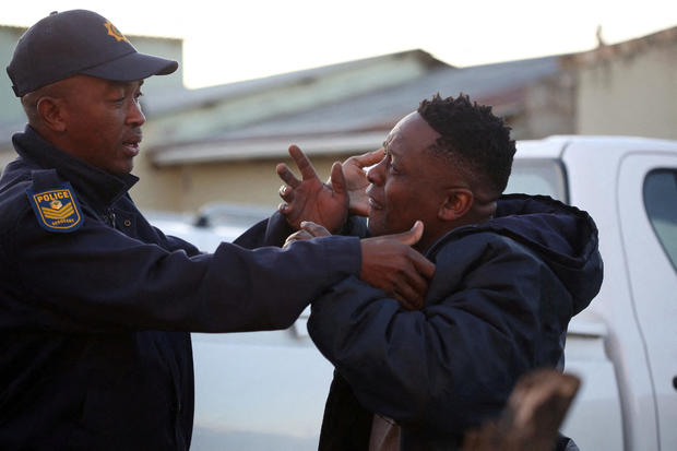 A family member reacts next to a police officer as forensic personnel investigate the deaths of patrons found inside the Enyobeni Tavern, in East London, South Africa, June 26, 2022. 