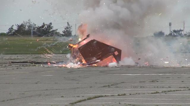 A dumpster burns in an empty parking lot as disposed fireworks go off 