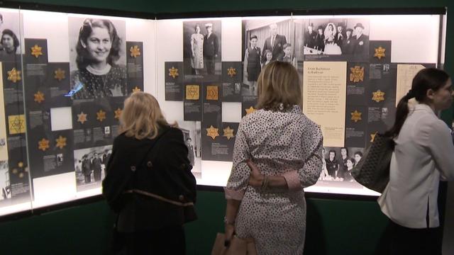 Visitors at the Museum of Jewish Heritage stand in front of a display case full of black-and-white photographs alongside Star of David patches 