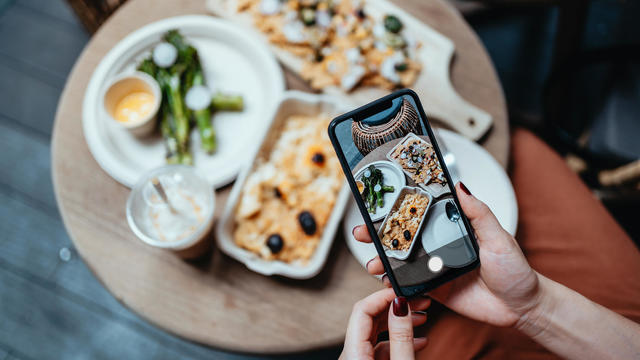 Personal perspective of young woman enjoying her home delivery takeaway meal in the balcony, taking photos of delicious food with smartphone before eating it. Eating in lifestyle. Camera eats first culture. Technology in everyday life 