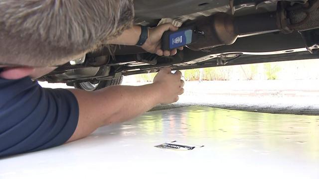 A man lies under a car and applied a label to a catalytic converter in order to etch a serial number inside 