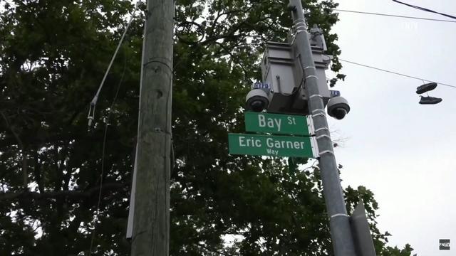 Two street signs are attached to a pole. The top reads "Bay St.," the bottom reads, "Eric Garner Way." 