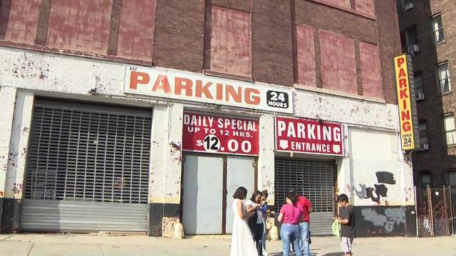 A group of people stand on the sidewalk outside a parking garage that has its gates down and doors closed. 