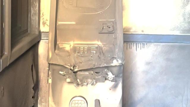An ATM that has been blackened by fire with pieces twisted and melted from the heat. 