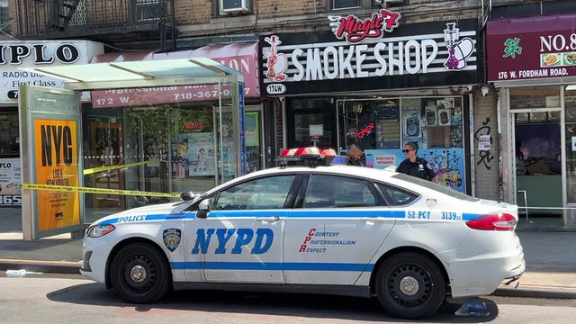 An NYPD vehicle is parked on the street outside Magic 7 Smoke Shop. Crime scene tape blocks off part of the sidewalk near the store. 
