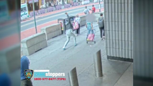 Surveillance video taken of a sidewalk in Times Square shows a woman walking down the street pulling a bag on wheels as a man behind her raises a box cutter over his head. 