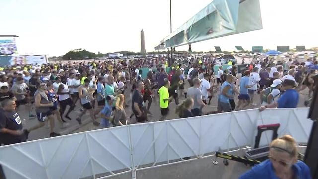 Dozens of runners cross the starting line at a race. 