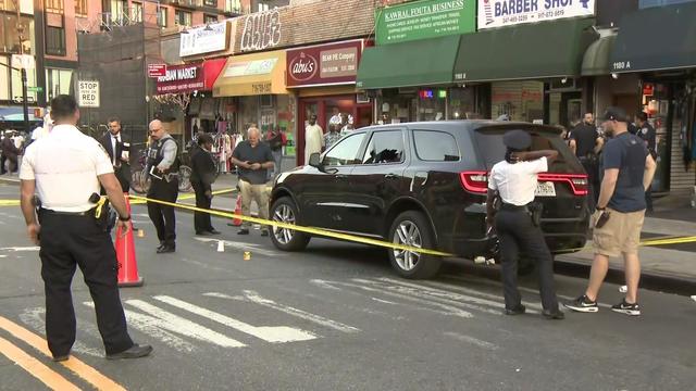 A black SUV with a shattered rear driver's side window is surrounded by police tape and orange cones. 