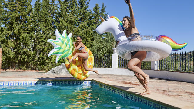 Two women jumping into the pool with float 