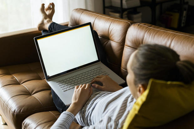 Young woman lying on couch at home using laptop 