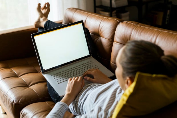 Young woman lying on couch at home using laptop