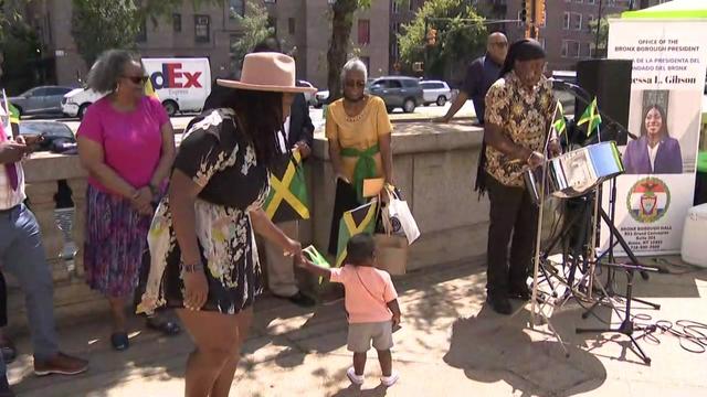 A woman and a child dance by a steel drum player. 