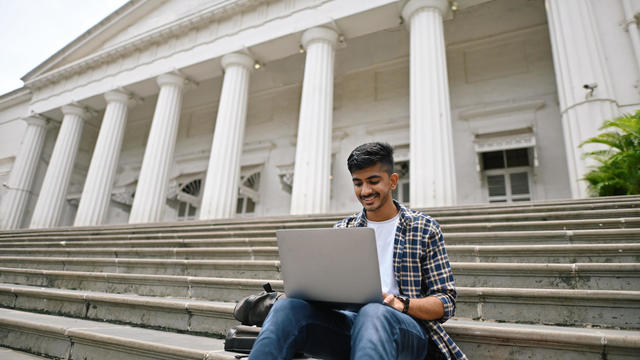 University student sitting outside on steps and using laptop 