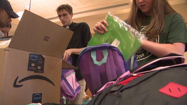 Volunteers put school supplies in backpacks. 