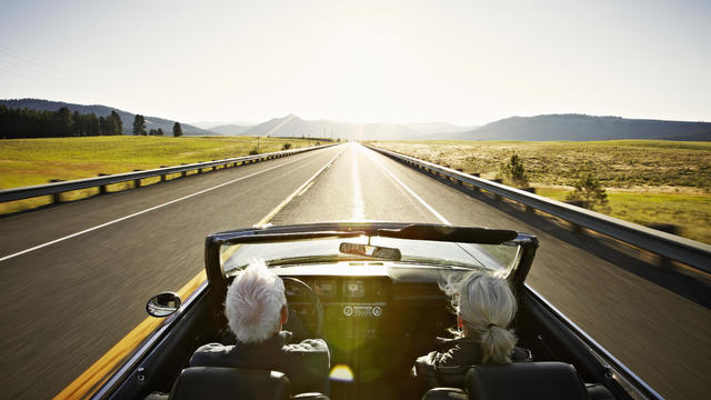 Senior couple driving convertible car at sunrise 