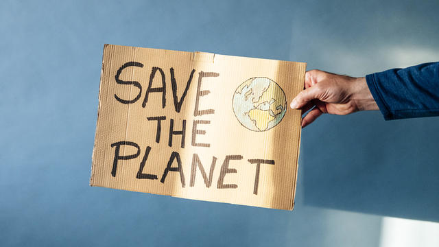 Man's hand holding a cardboard sign that says SAVE THE PLANET 