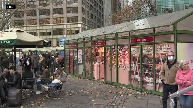 People sit at tables in Bryant Park near pop-up holiday shops. 