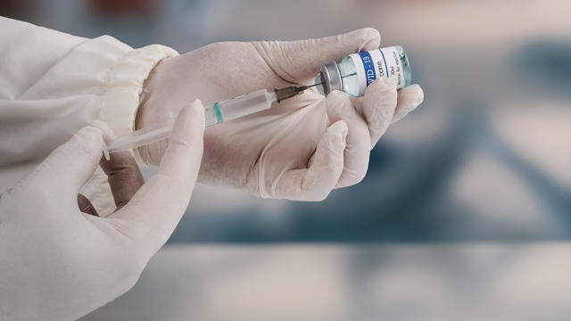 A young doctor in white protective glove is holding a medical syringe and vial 