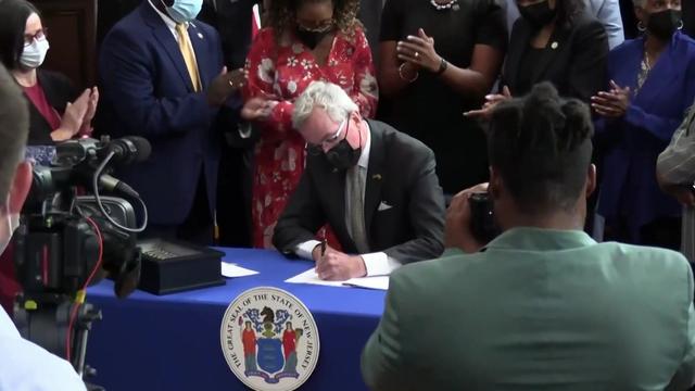 Gov. Phil Murphy sits at a table signing legislation. 