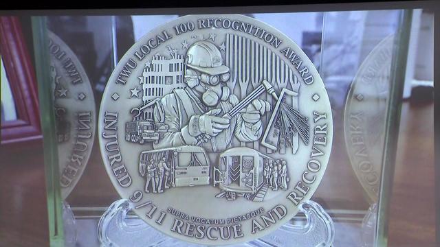A medal reading "TWU Local 100 Recognition Award; Injured 9/11 Rescue and Recovery." 