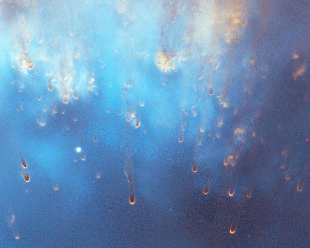 Bright light blue covers most of the image. What appear to be raindrops start toward the top of the image, shown in light orange-pink, and trail down the scene, which is a clip of a larger image of the Helix Nebula. 
