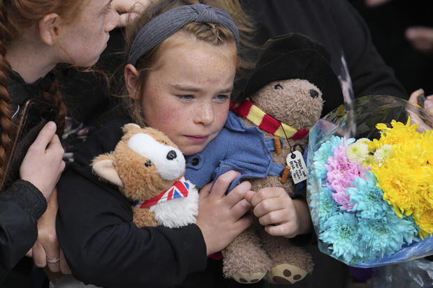 A young girl holds a Paddington bear and a Corgi dog stuffed toys while waiting to watch the Procession of Queen Elizabeth's coffin from the Palace of Holyroodhouse to St Giles Cathedral on the Royal Mile