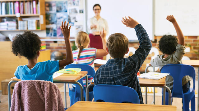 Shot of an unrecognizable group of children sitting in their school classroom and raising their hands to answer a question 