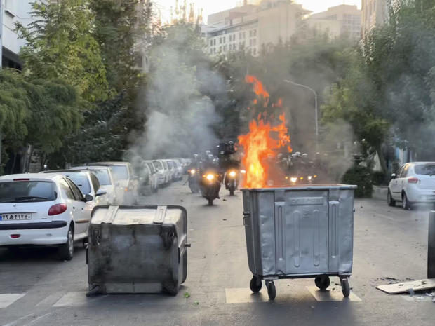 In this Sept. 20, 2022, photo taken by an individual not employed by the Associated Press and obtained by the AP outside Iran, a trash bin is burning as anti-riot police arrive during a protest over the death of a young woman who had been detained for violating the country's conservative dress code, in downtown Tehran