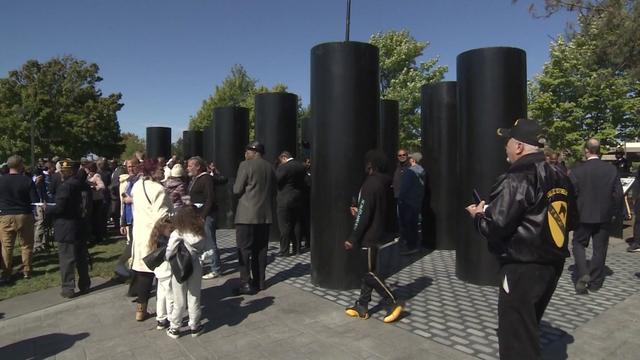 People walk amongst a monument made up of tall black columns. 