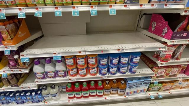 A full shelf of baby formula underneath a completely bare shelf of other types of baby formula. 