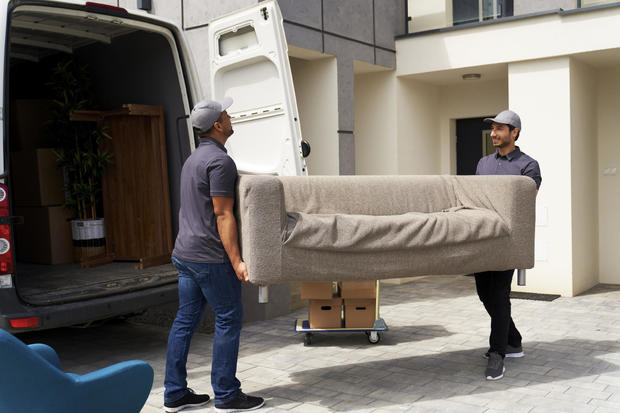 Male delivery coworkers unloading sofa from moving van near house 