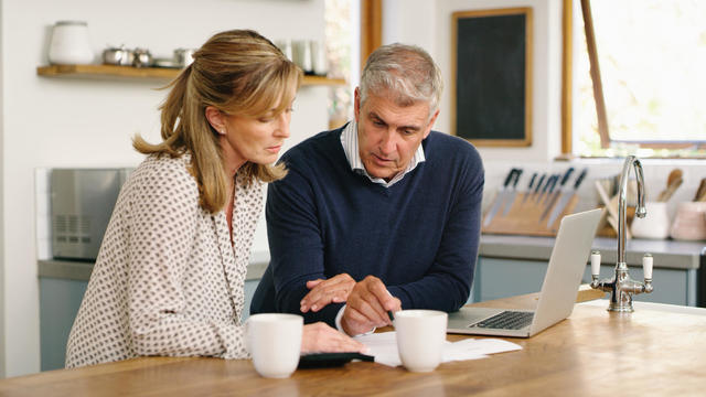 A senior couple planning their finance and paying bills while using a laptop at home. A mature man and woman going through paperwork and working online with a computer 