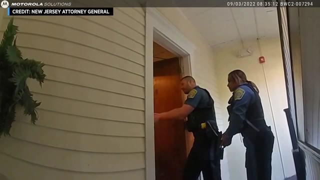 Two Englewood Police officers stand outside a home with their weapons drawn. 
