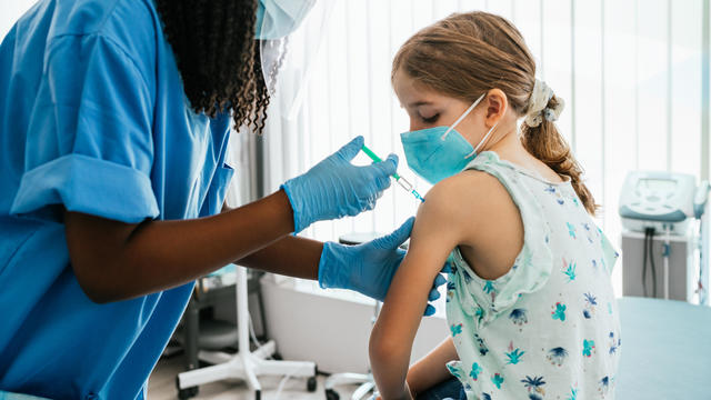 Young girl watching her being injected with COVID-19 vaccine at a medical clinic 