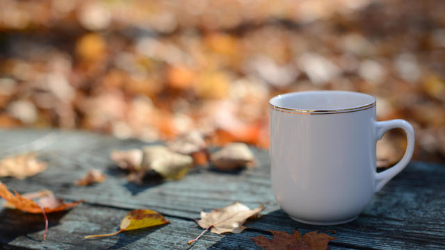 Close-up of coffee cup with autumn leaves on table 