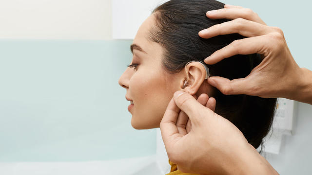 Installation hearing aid on woman's ear at hearing clinic, close-up, side view. Deafness treatment, hearing solutions 