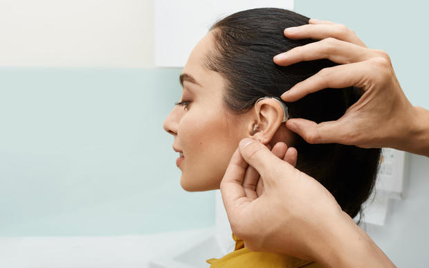 Installing hearing aid on woman's ear in hearing clinic, closeup, side view.  Deafness treatment, hearing solutions 