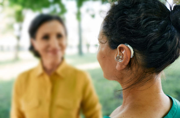 Hearing impaired adult woman uses a hearing aid to communicate with her female friend in a city park.  Hearing solution 