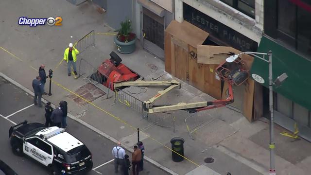 A piece of construction equipment lays on its side in a partially collapsed sidewalk. 