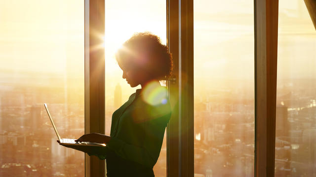 Businesswoman on laptop at window in morning sun 