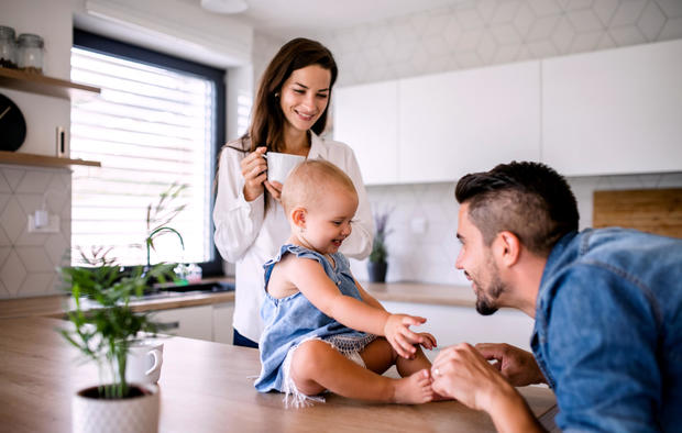 Portrait of young couple with toddler girl standing indoors in kitchen at home. 