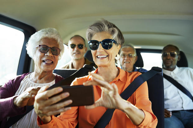 Smiling woman using smartphone from friend in car 