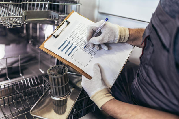 Male Technician Sitting Near Dishwasher Writing On Clipboard In Kitchen 