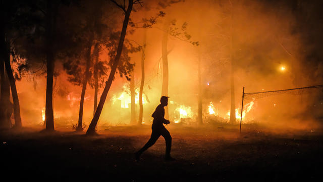 A man runs past a burning forest to help save homes during a 