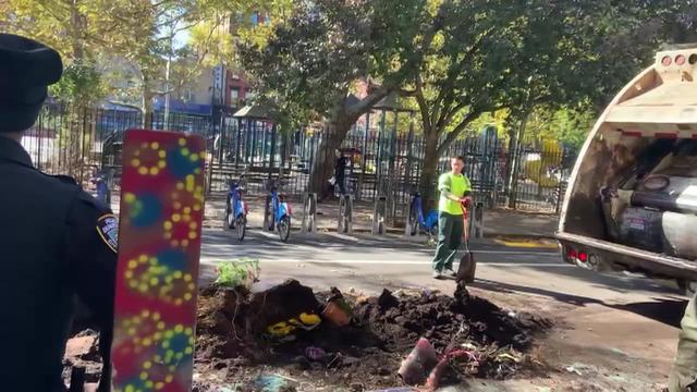 A worker with a shovel stands near a pile of debris behind a garbage truck. 