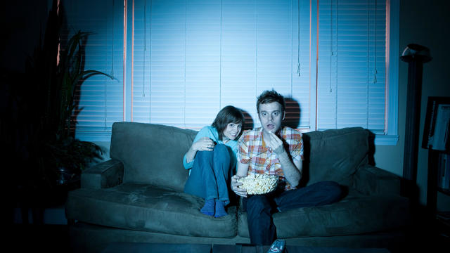 Young couple watching tv, man eating popcorn 