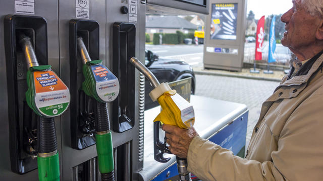 Elderly man selecting diesel fuel pump nozzle and watching expensive price at fuel dispenser of gas station for refueling his car in Belgium. 